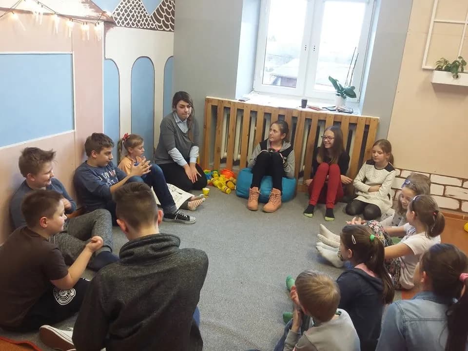 Zdjęcie przedstawia dzieci z placówki siedzące na dywanie podczas zajęć, wraz z osobą prowadzącą.