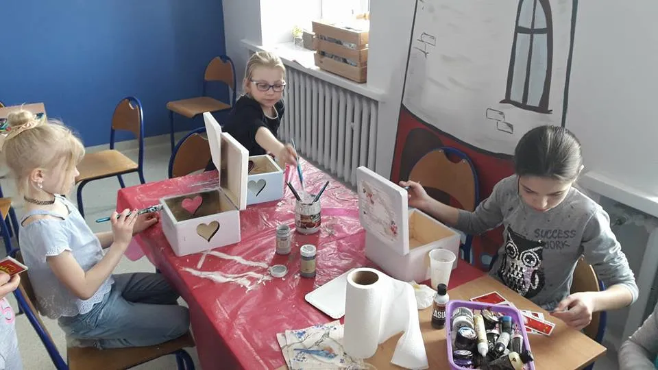 Obraz przedstawia wychowanków SPWD podczas warsztatów artystycznych. Na zdjęciu można ujrzeć proces tworzenia drewnianych skrzyneczek.