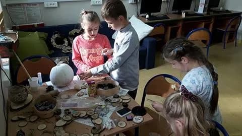 Zdjęcie przedstawia dzieci tworzące dekorację z rzeczy znalezionych w lesie, np. szyszki, mech, itd.