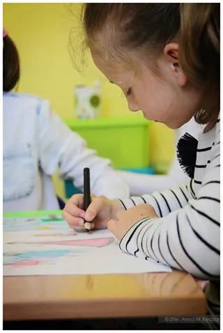 Zdjęcie przedstawia dziewczynkę malującą obrazek czarną kredką.