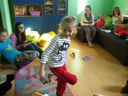 Zdjęcie przedstawia wnętrze jednego z pokoi w którym dzieci spędzają czas, również one są tam obecne wraz z opiekującymi się nimi osobami.