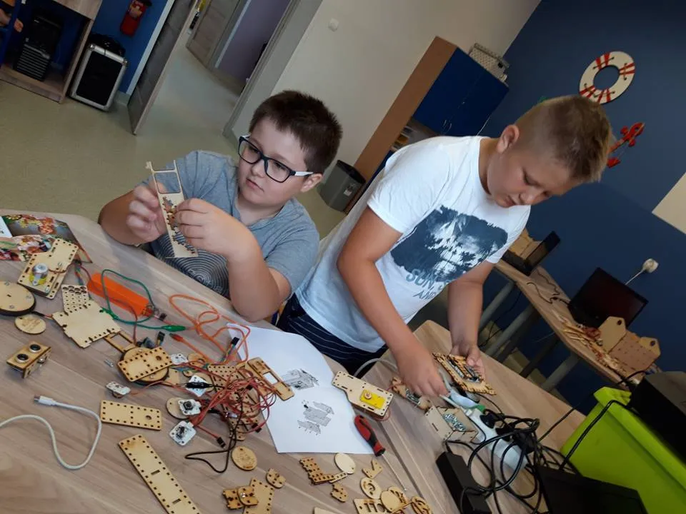 Obraz przedstawia warsztaty robotyki. Na zdjęciu możemy ujrzeć dzieci, które tworzą roboty.