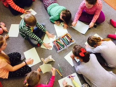 Zdjęcie przedstawia dzieci malujące na kartkach siedząc na dywanie. Zdjęcie jest zrobione z góry.