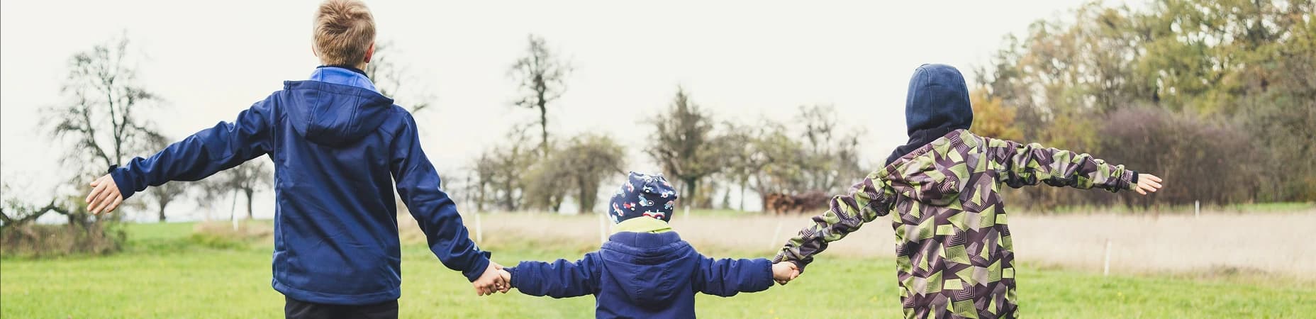 Trójka dzieci biegnących przez łąkę w kurtkach