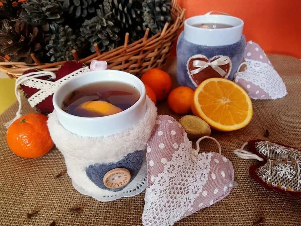 Zdjęcie ozdobne z ozdobionymi kubkami herbaty, a na tle koszyk z szyszkami.