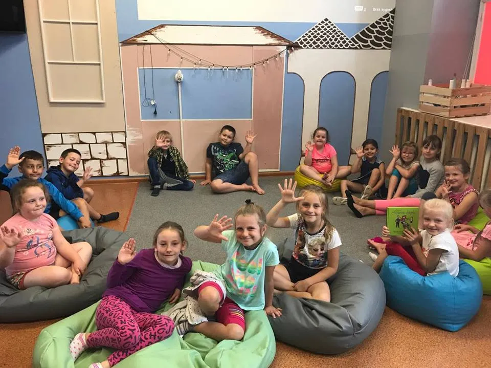 Zdjęcie przedstawia dzieci siedzące na specjalnych rzeczach do siedzenia w pokoju z niebieskimi ścianami oraz dekoracją w kształcie domku.