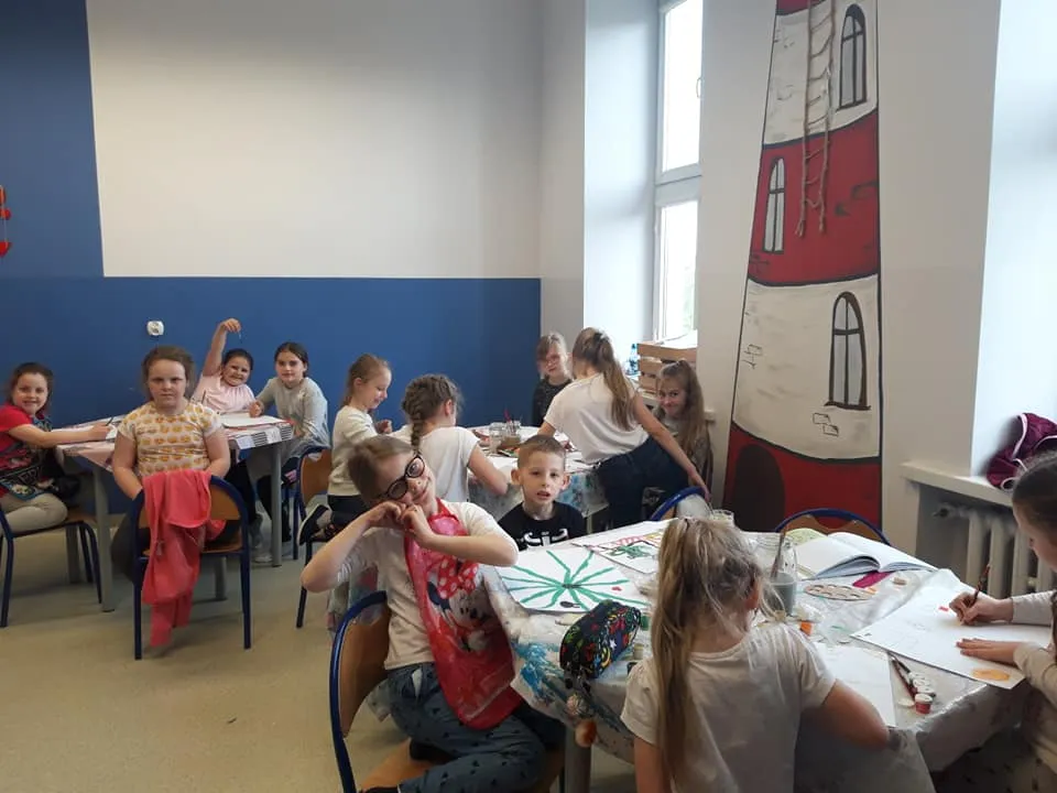 Obraz przedstawia naszych wychowanków podczas zajęć z bezpieczeństwa w internecie. Na zdjęciu widzimy dzieci siedzące przy stołach na których wykonują rysunki.