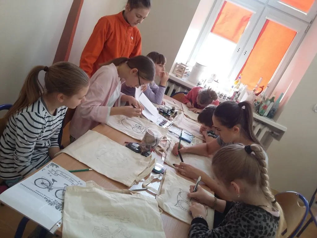 Zdjęcie przedstawia dzieci z placówki przy stole malujące na płótnach.