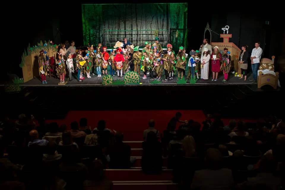 Obraz przedstawia salę teatralną z widownią, na scenie widnieją aktorzy jak i dzieci z placówki, które brały w tym dniu udział w przedstawieniu.