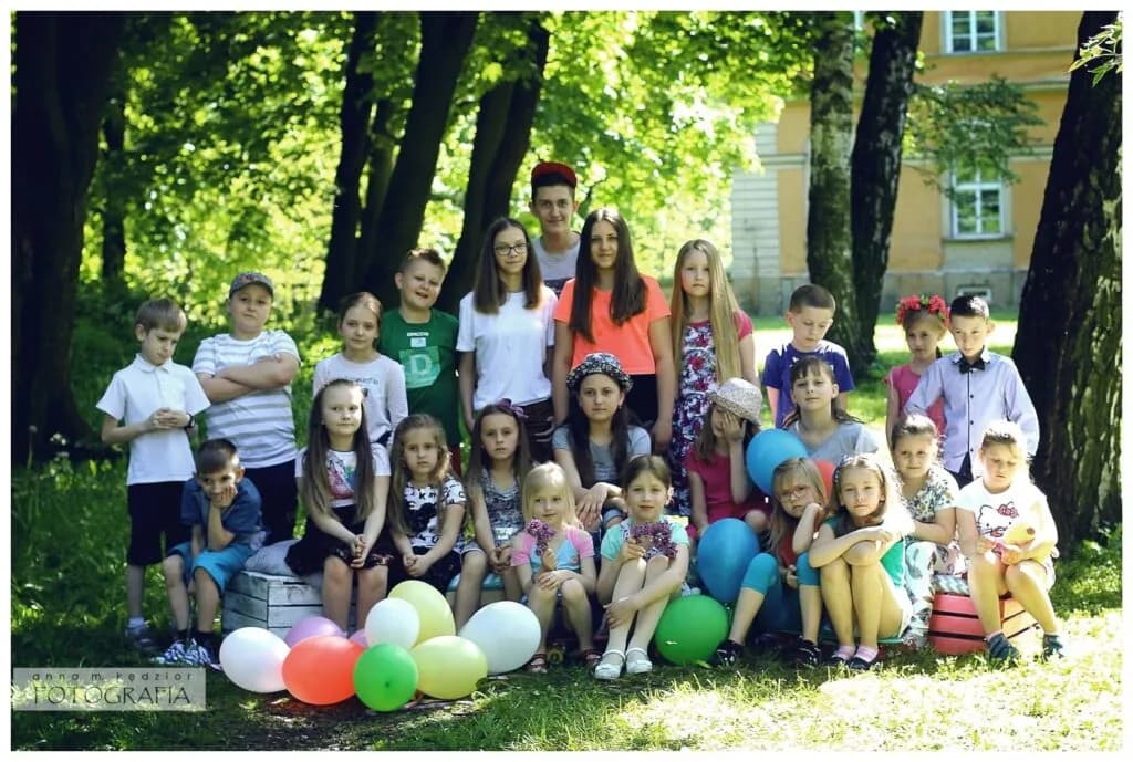 Zdjęcie przedstawia dzieci z placówki a na tle pałac (dawna szkoła) wśród drzew.